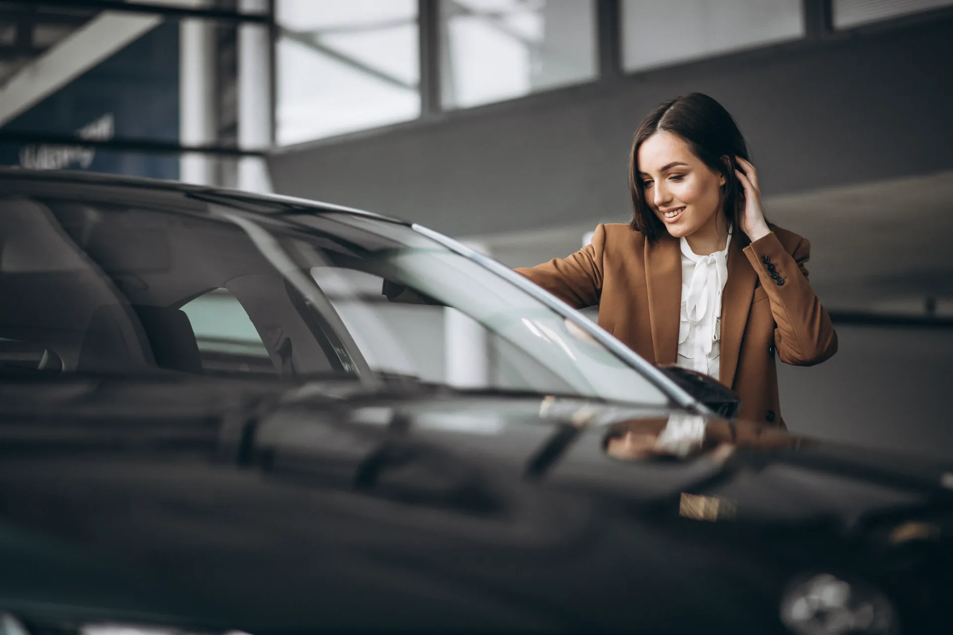 mujer joven eligiendo coche en sala de exposición de automóviles